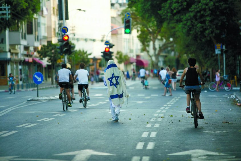יום כיפור: אחד עם טלית בדרך לבית הכנסת ואחרים על אופניים. צילום: עופר וקנין